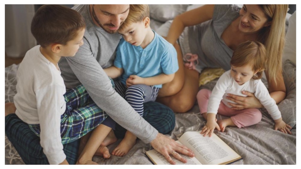 Family in pajamas on a bed around a book